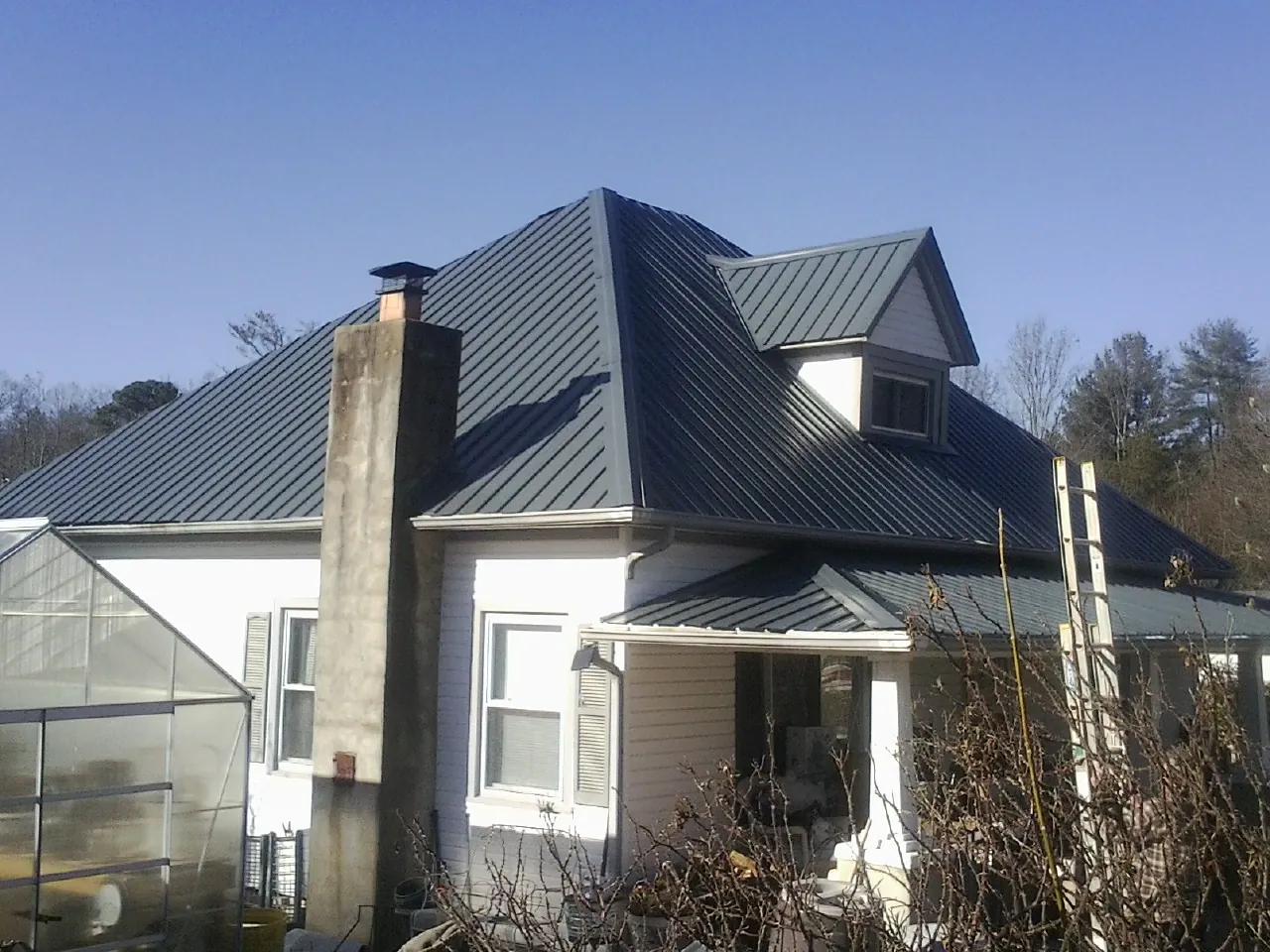 Dark blue standing seam metal roof on a white farmhouse with dormer — Slate & Tile Roof Repair by Roofing Brothers in Cadillac