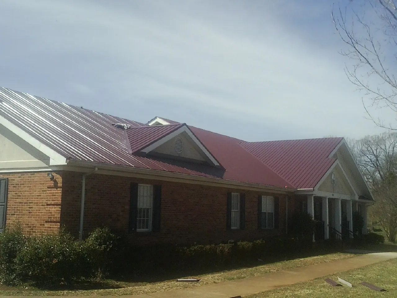 Red metal roof with gabled entries on a long brick building, from a Hail Damage Roof Repair job in Cadillac