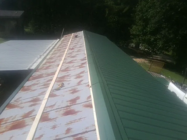Old rusted panels beside newly installed green metal roofing — Wind Damage Roof Repair by Roofing Brothers in Cadillac