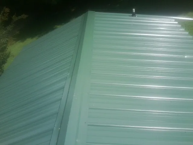 New green metal panels meeting at the ridge of a roof — Flat Roof Repair work by our crew in Cadillac