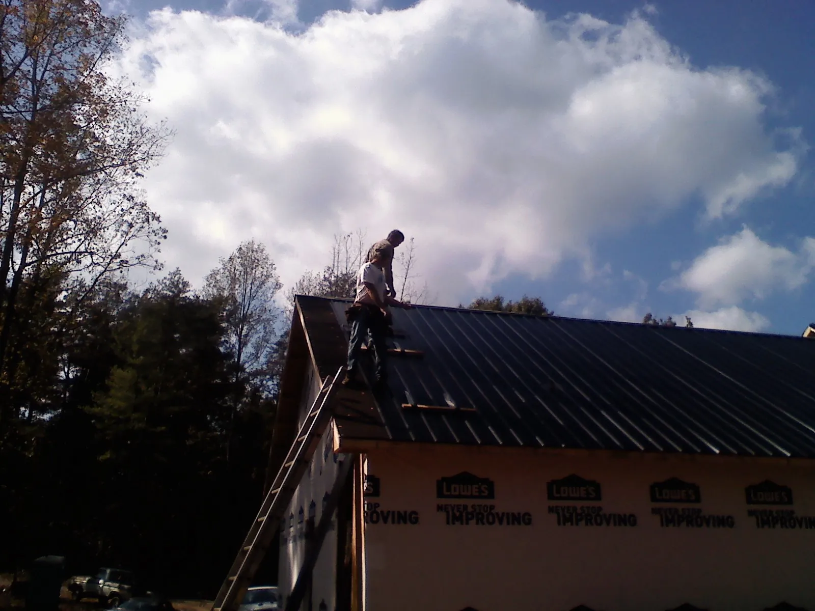 Roofer fastening dark metal panels high against a cloudy sky, from a Roof Inspection job in Cadillac