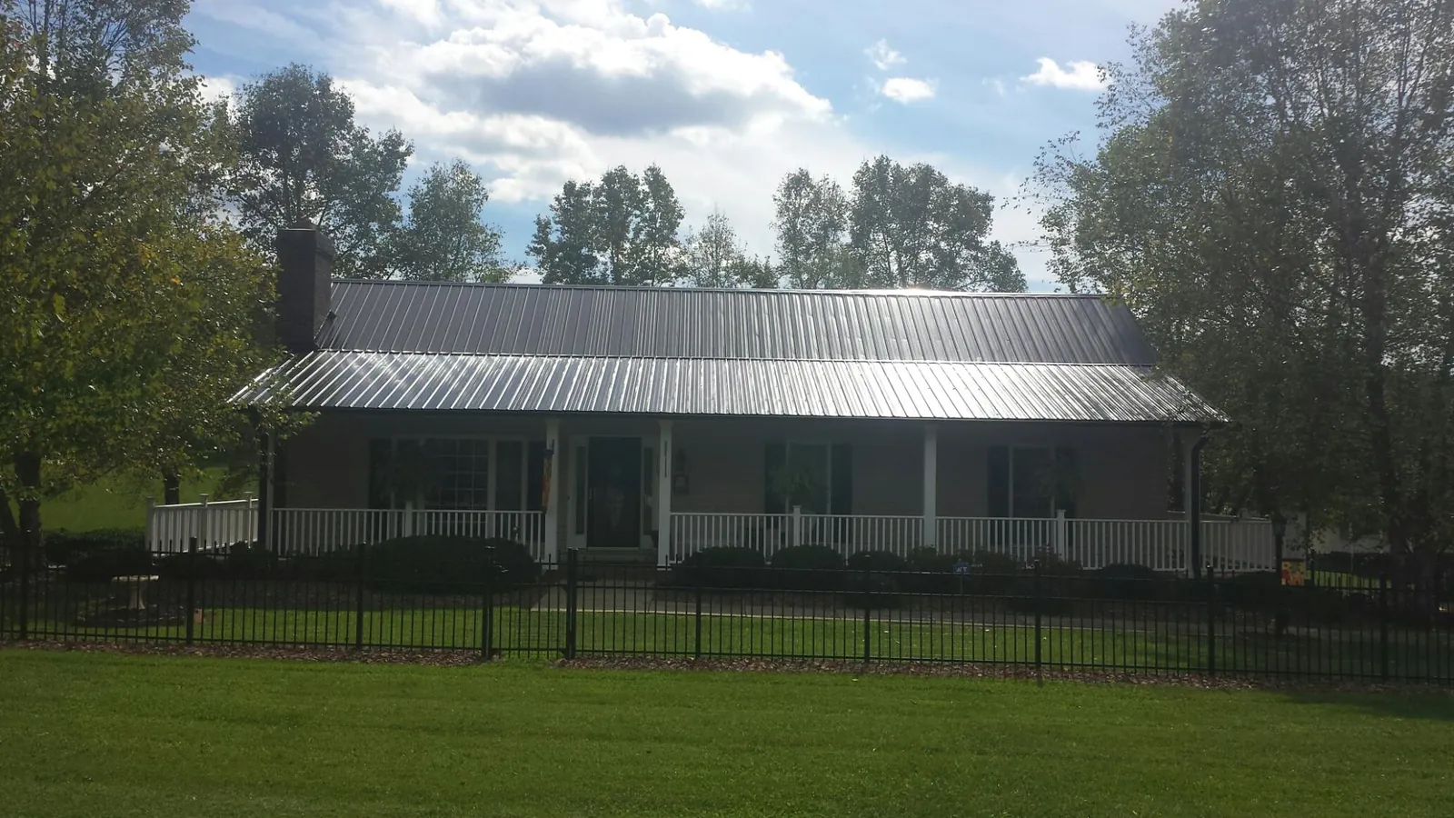 Gray metal roof on a brick ranch with a full width front porch — Gutter Guard Installation work by our crew in Cadillac