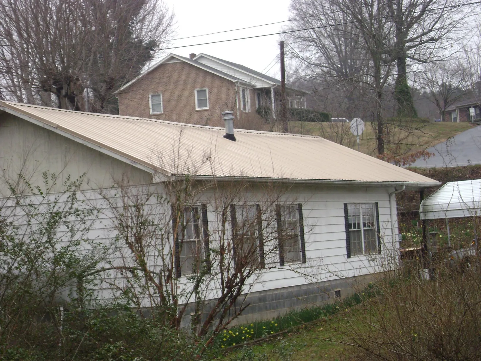 Tan metal roof on a white sided house set into a hillside — Commercial Roofing by Roofing Brothers in Cadillac