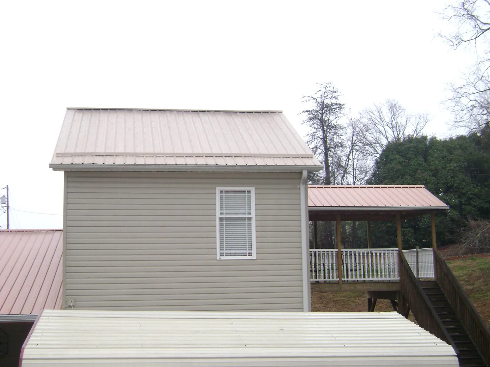 Tan metal roofs on a two story addition and attached porch, from a Roof Replacement job in Cadillac